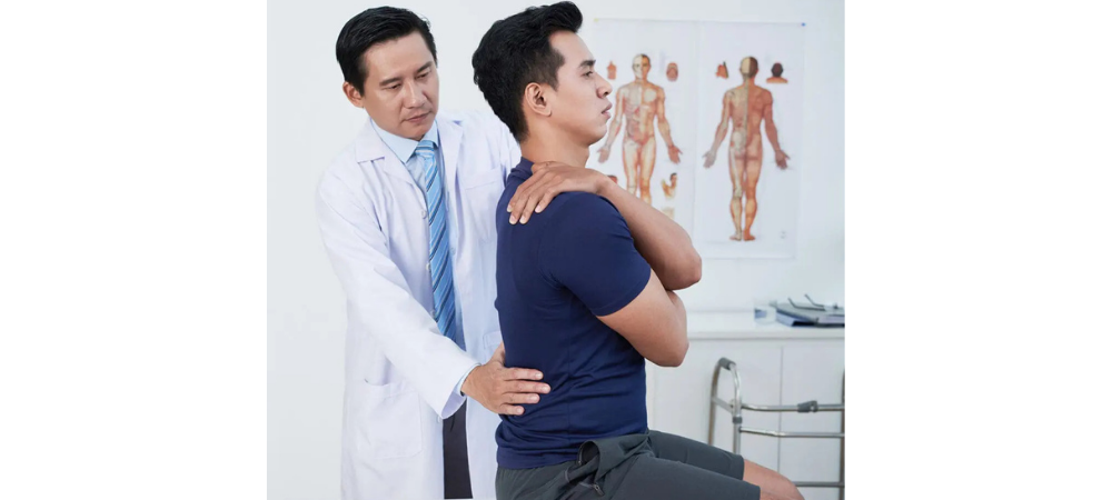 patient sitting on treatment table with arm over shoulder, doctor palpating lower back