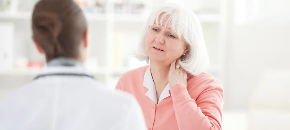 elderly woman with hand on her neck, talking to doctor