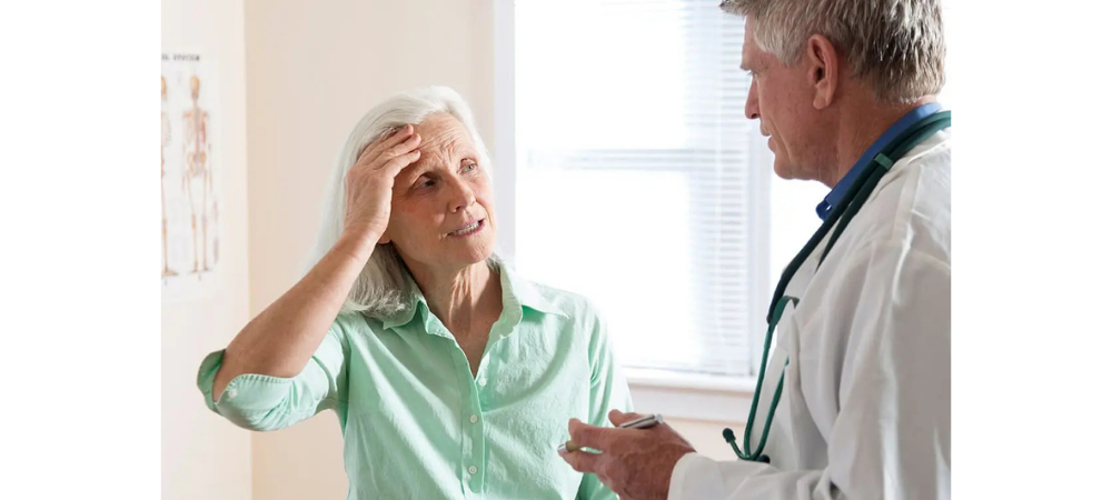 elderly woman with her hand on her forehead, talking to doctor