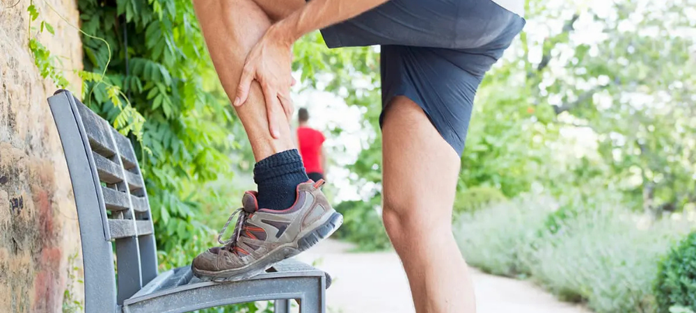 man on nature trail lifting his leg onto bench showing ankle pain
