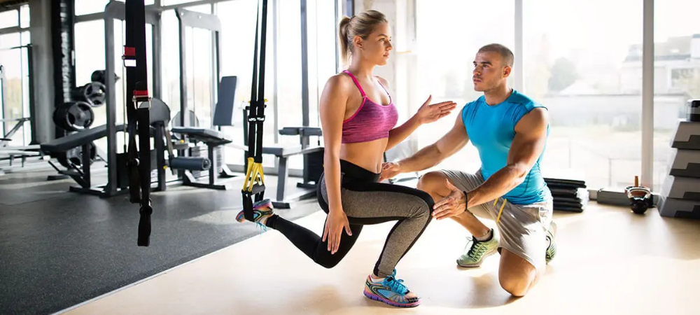 woman in athletic wear lunging with one leg up, trainer next to her