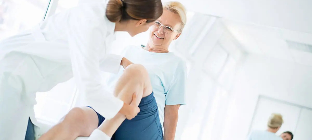 older woman sitting on table, doctor manipulating her knee