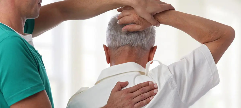 doctor pulling elder patient arm over his head, testing range of motion